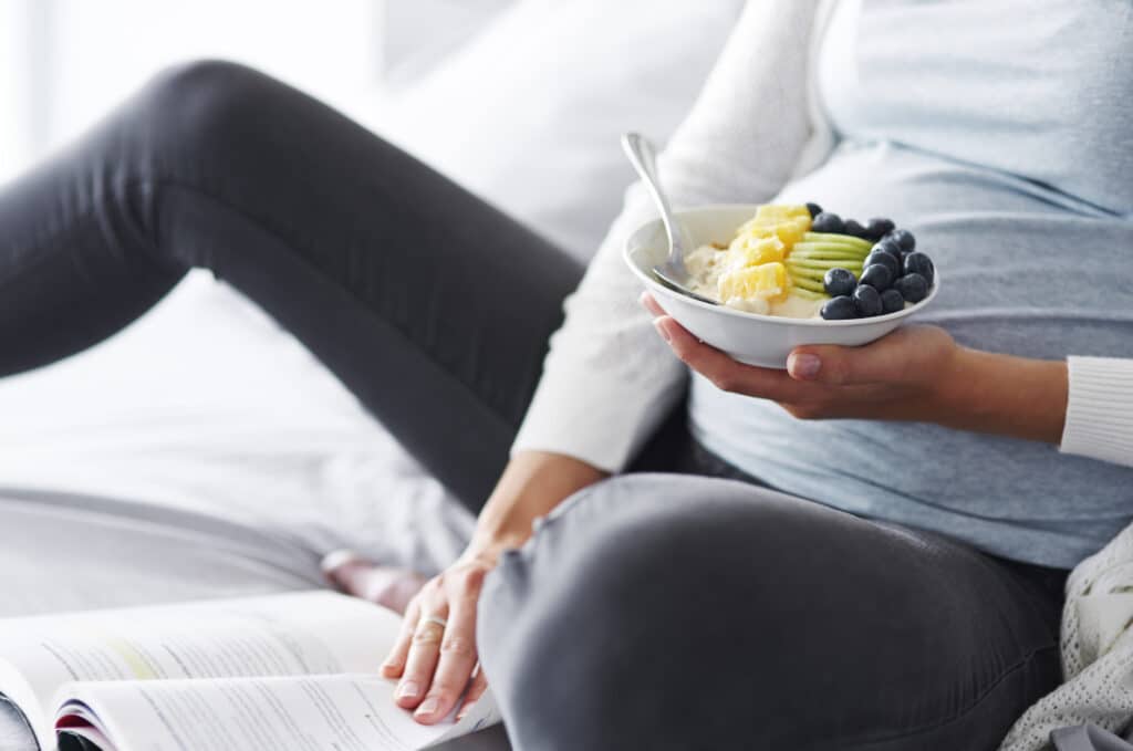 pregnant woman eating bowl of healthy fruit
